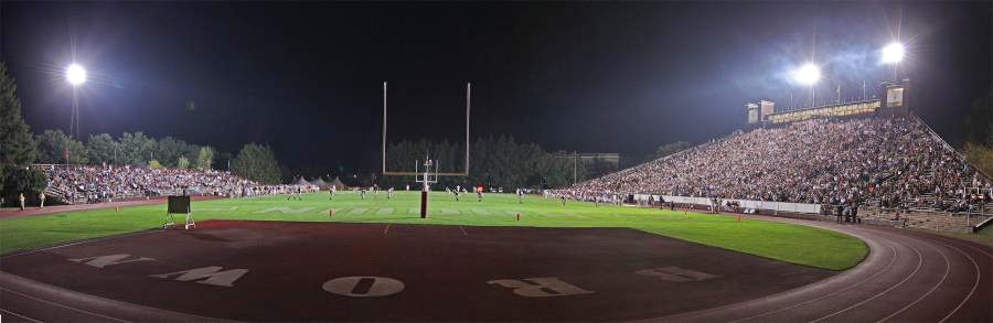 wide angle view of a football field and crowded stands at night