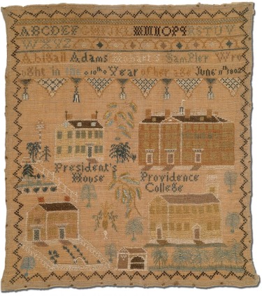 A brown fabric with a needlepoint design including letters, names, and a landscape of Providence buildings framed by a decorative edge.