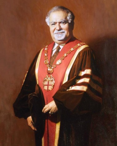 full standing portrait of a bearded older adult wearing doctoral black robes with a red sash