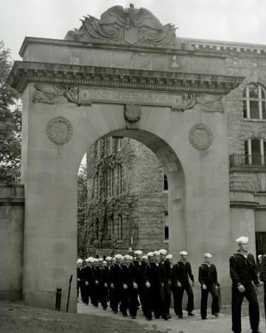 A black and white photograph of Brown students in Naval uniform marching out of the War Memorial Gate in formation