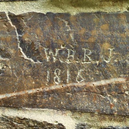 A rough stone wall with letters and years carved into the stone.