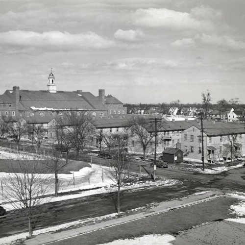 A black and white photograph of a row of dormitory buildings with winter trees and slightly snowy streets.