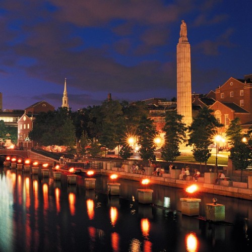 A view of the canal at night, with bright red light from fire and yellow light from street lamps illuminating the purple sky.