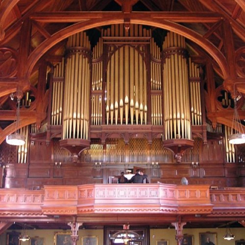 A photo of the Sayles organ, with its gold-yellow pipes pointing to the ceiling, surrounded by reddish wood.